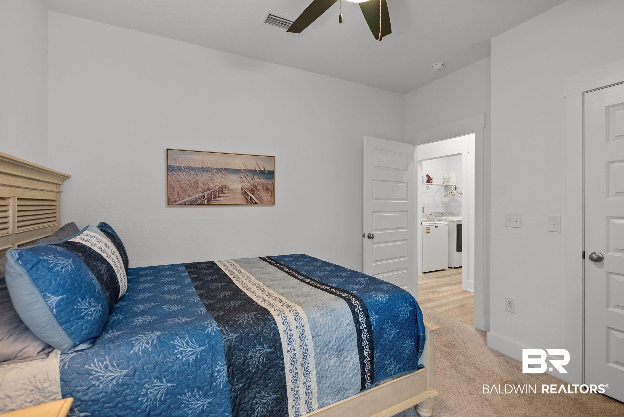 9899 Willet Way Foley, AL 36535 - Photo 23 of 37 Carpeted bedroom with a ceiling fan, white paneled doors, and an adjacent utility room featuring laundry appliances and wood-finish flooring