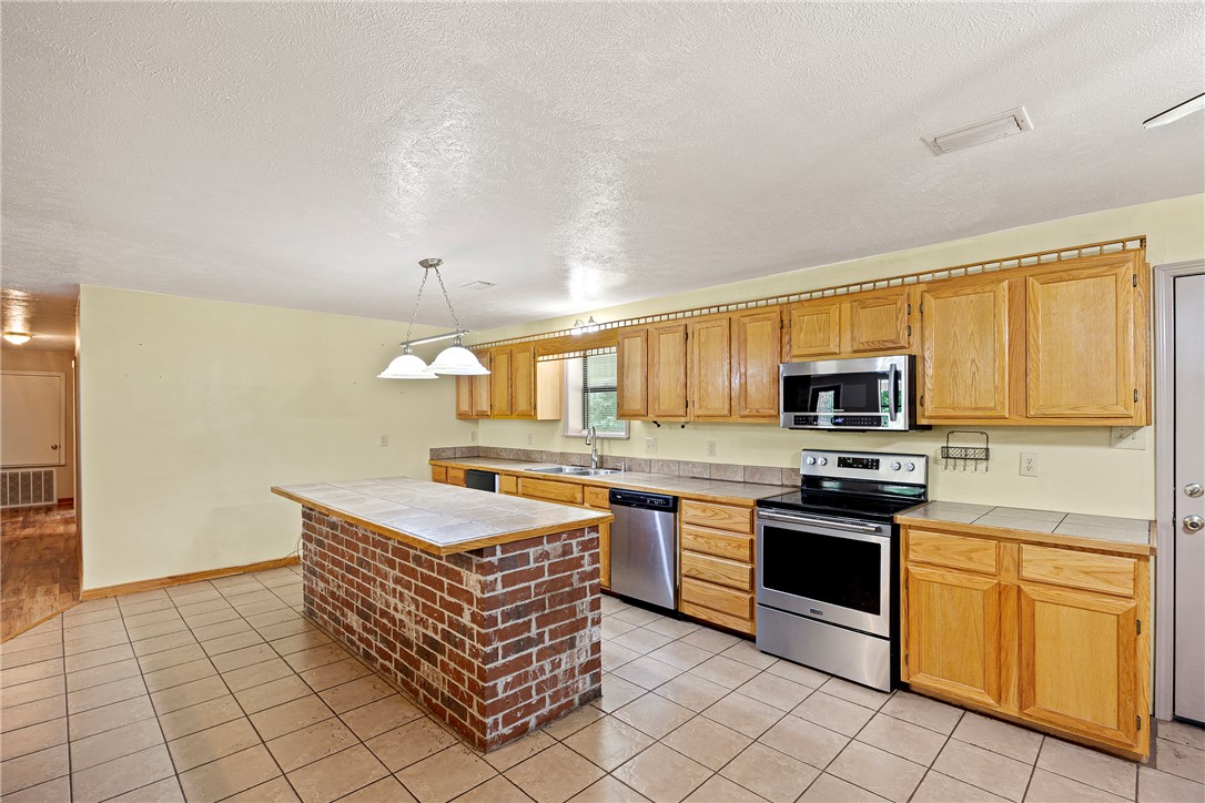655 Charton Road Morrilton, AR 72110 - Photo 12 of 49 Kitchen featuring a brick island with a tiled countertop, stainless steel appliances, wood-finish cabinetry, and tiled flooring