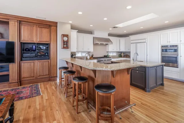 a kitchen with stainless steel appliances granite countertop a stove top oven a sink dishwasher a dining table and chairs with wooden floor