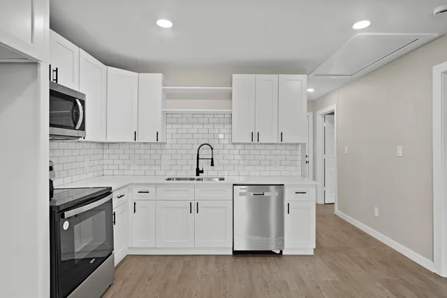 a kitchen with stainless steel appliances granite countertop a sink stove a refrigerator and white cabinets with wooden floor