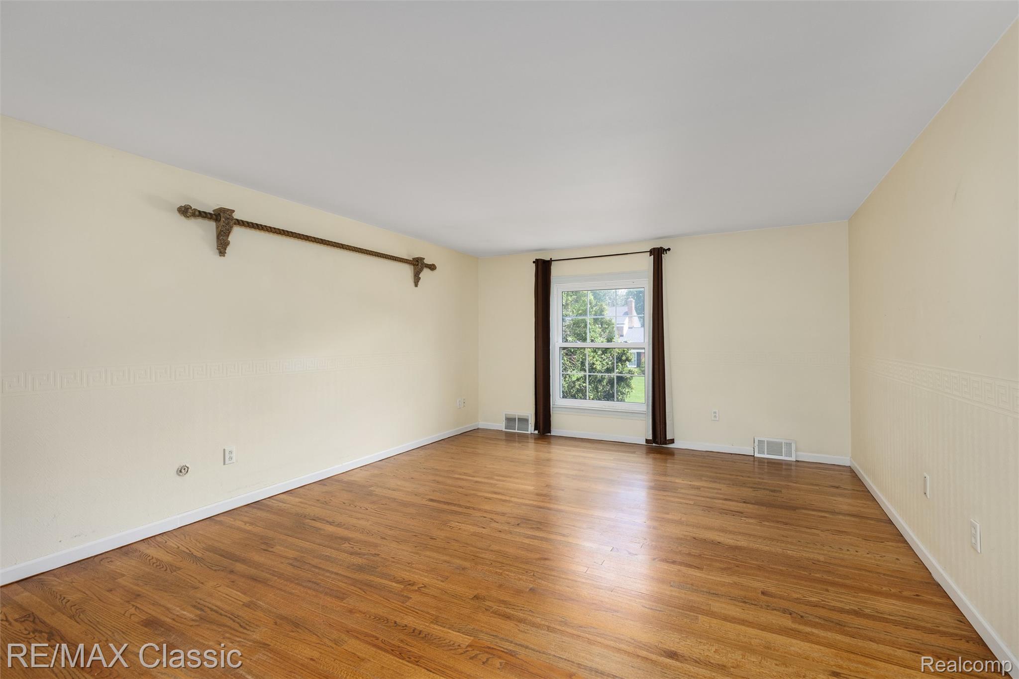 4268 Covered Bridge Road Bloomfield Hills, MI 48302 - Photo 13 of 35 Spacious room featuring wood-finish flooring, a large window with dark curtain rods, light-toned wall finishes, and white baseboards