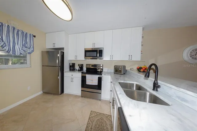 a kitchen with stainless steel appliances granite countertop a refrigerator a stove a sink and a white wooden cabinets