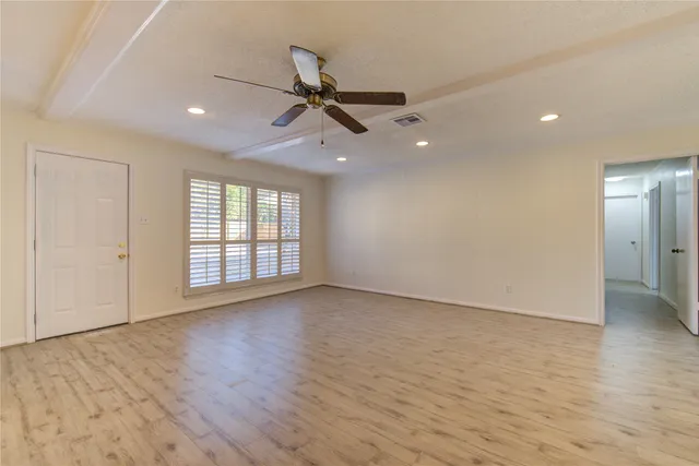 an empty room with wooden floor fan and windows