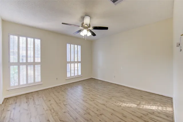an empty room with wooden floor fan and windows