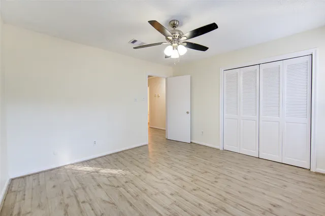 an empty room with wooden floor closet and fan