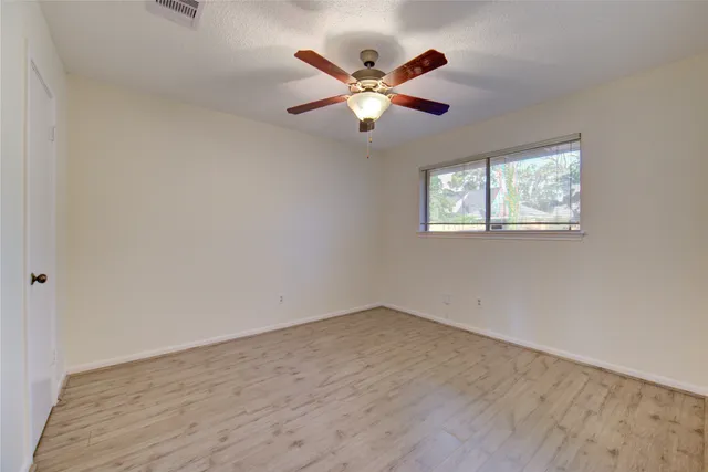 a view of an empty room with wooden floor and a ceiling fan