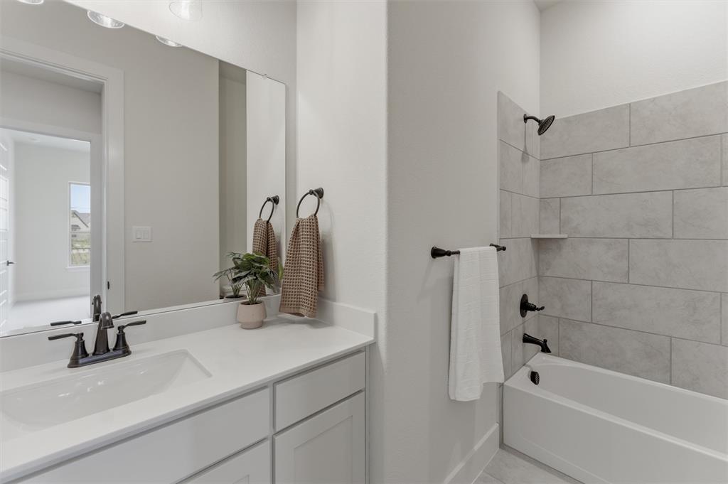 2433 Meteor Drive Krum, TX 76249 - Photo 7 of 29 Bathroom featuring a single vanity with a white countertop and integrated sink, matte black faucet, and a shower-tub combination with light grey tile surround