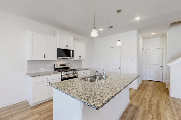 a view of an empty room and kitchen with wooden floor
