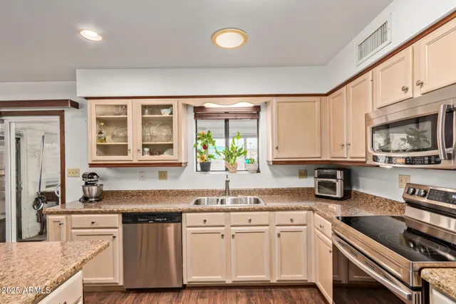 a kitchen with stainless steel appliances granite countertop a stove top oven a sink dishwasher a refrigerator and a dining table with wooden floor