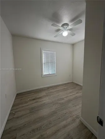 an empty room with wooden floor fan and windows