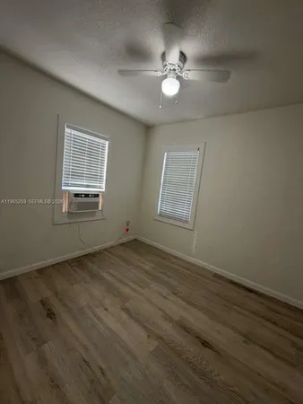 an empty room with wooden floor fan and windows