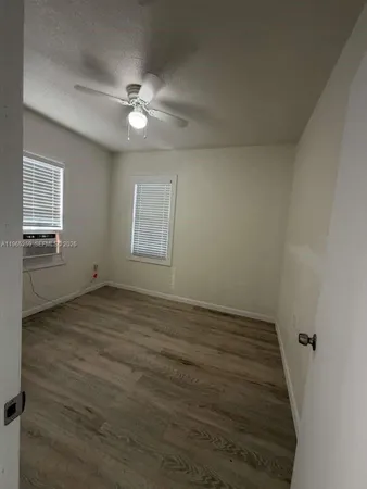 an empty room with wooden floor fan and windows