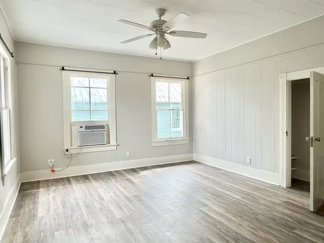an empty room with wooden floor chandelier fan and windows