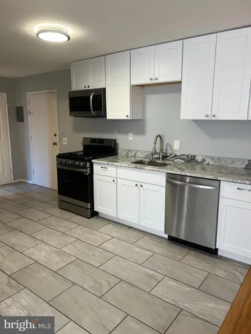 a white kitchen with granite countertop a stove top oven a sink a counter space and cabinets