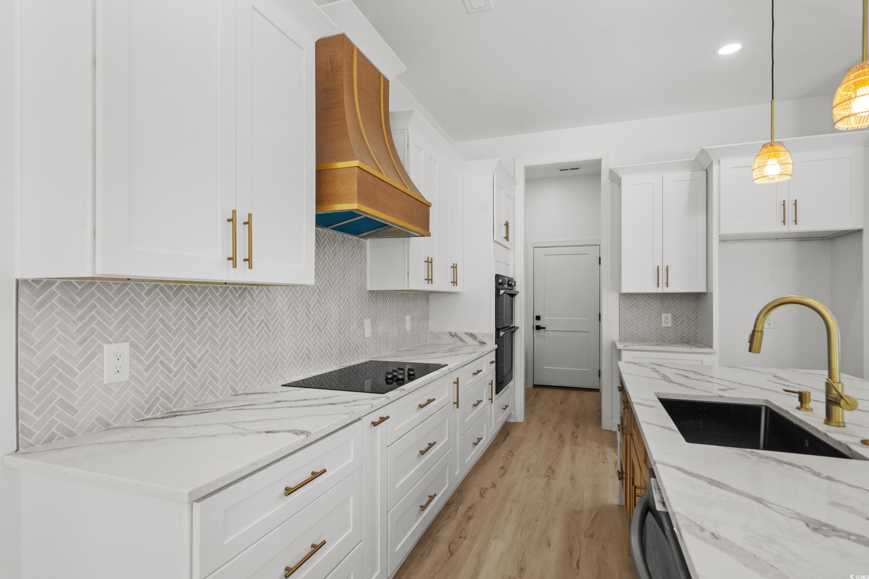 232 Ole Maple Street Loris, SC 29569 - Photo 9 of 40 Kitchen with light stone counters, light wood-style floors, white cabinetry, pendant lighting, and decorative backsplash