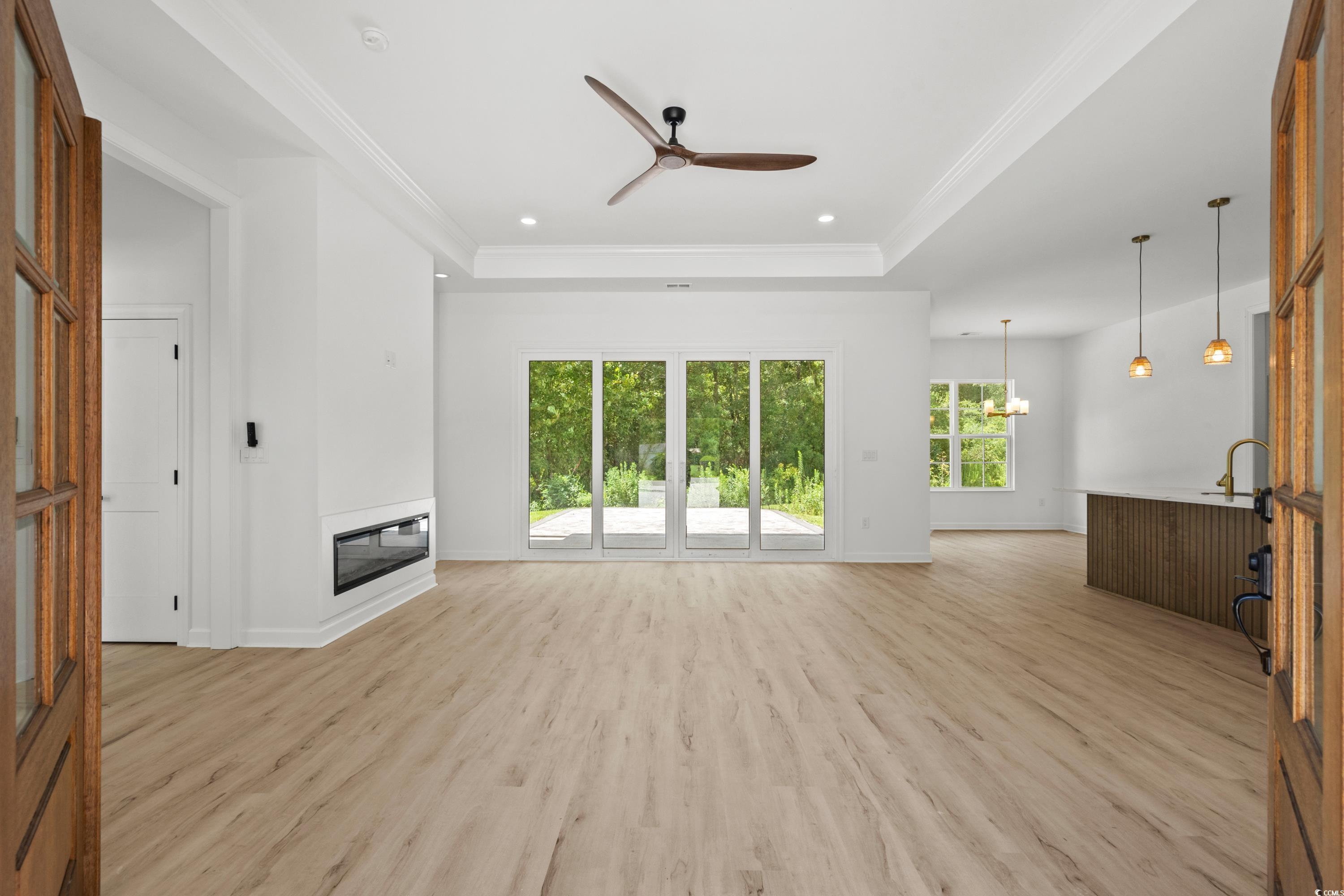 232 Ole Maple Street Loris, SC 29569 - Photo 6 of 39 Unfurnished living room with light wood-style floors, a tray ceiling, ceiling fan, ornamental molding, and a glass covered fireplace