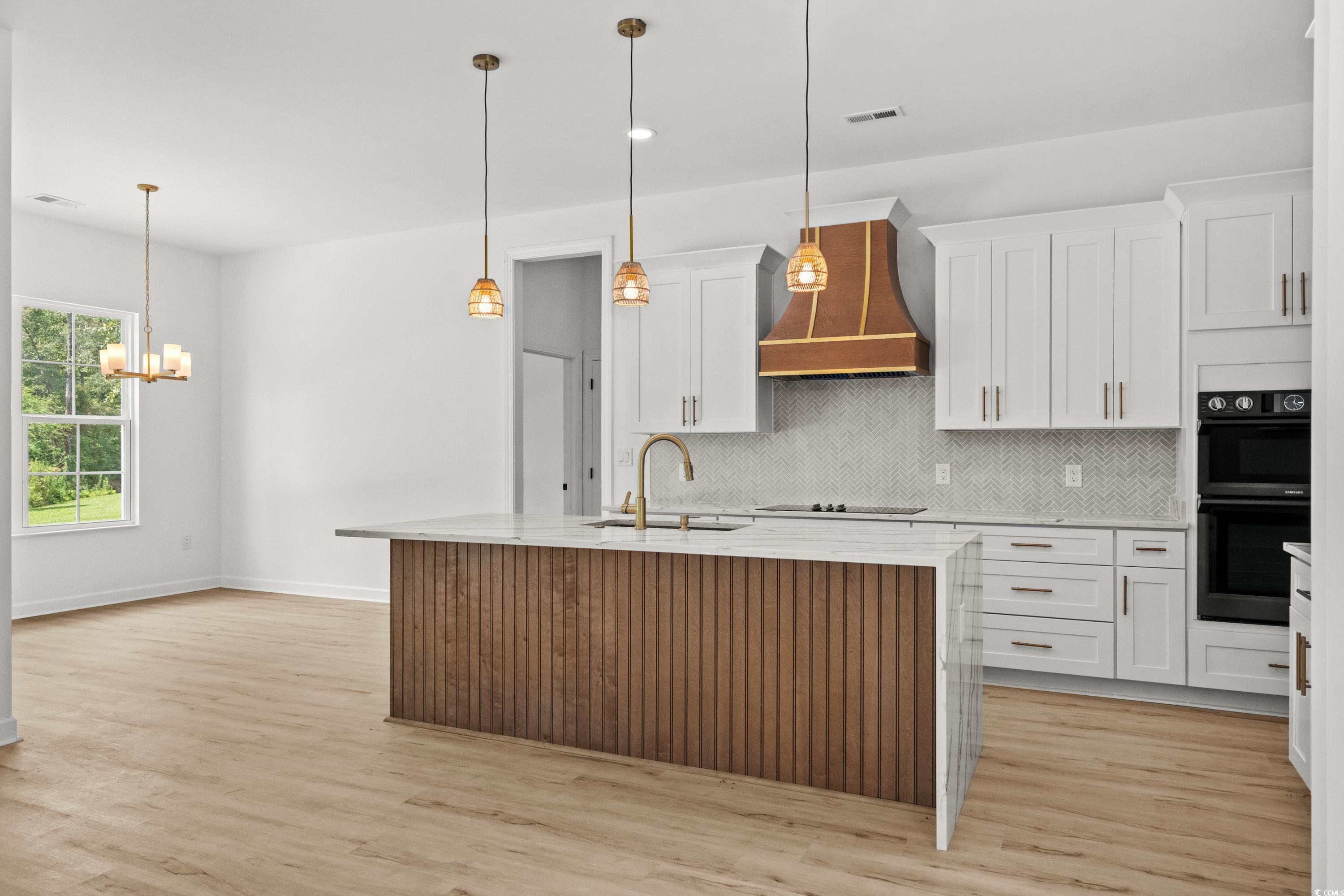232 Ole Maple Street Loris, SC 29569 - Photo 7 of 40 Kitchen featuring light stone countertops, backsplash, hanging light fixtures, a center island with sink, and light wood-style flooring