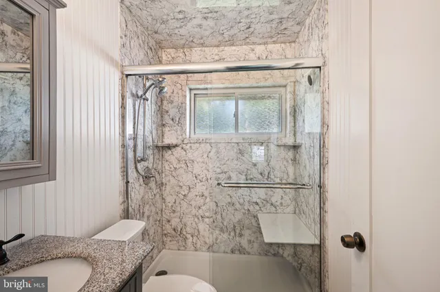 a bathroom with a granite countertop sink a toilet and shower