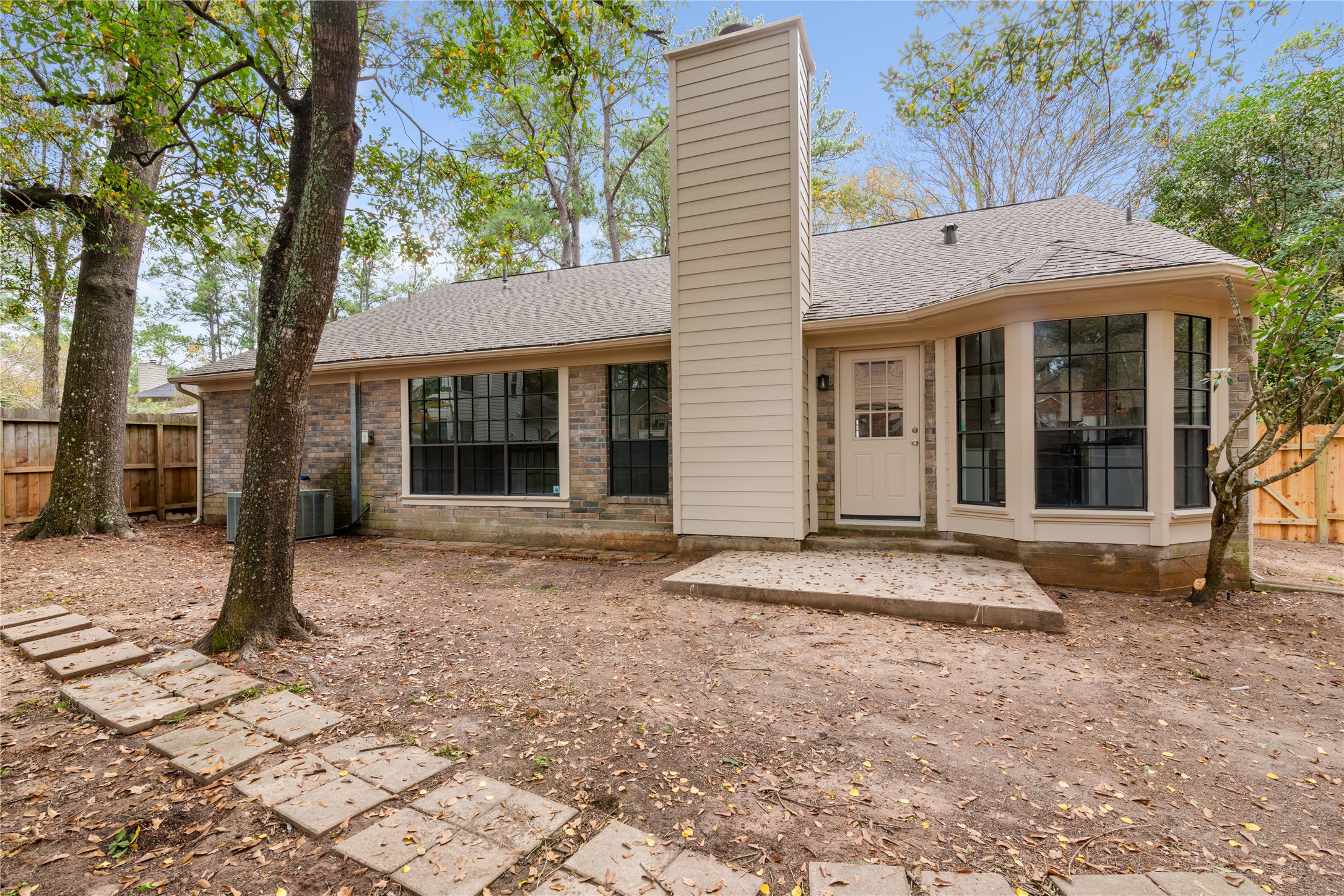 10 White Fawn Drive Spring, TX 77381 - Photo 24 of 25 This cozy home features a charming backyard with mature trees and a paved walkway. The exterior showcases a mix of brick and siding, with large windows and a bay window adding character. A secure wooden fence provides privacy, making it an inviting space for relaxation.