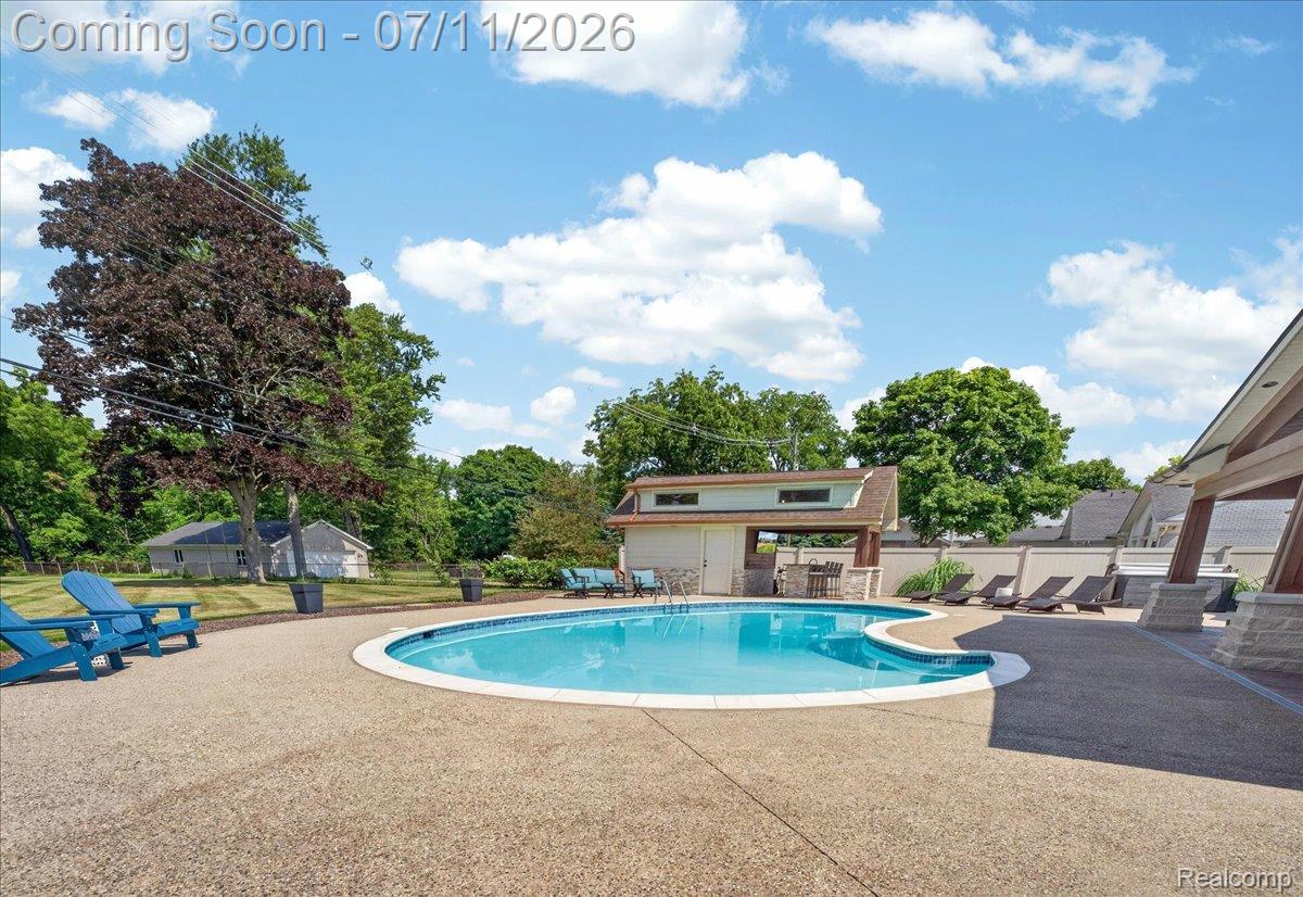23750 East River Road Grosse Ile, MI 48138 - Photo 34 of 54 Outdoor swimming pool with an exposed aggregate deck, a pool house featuring a covered outdoor kitchen, and surrounding landscaping