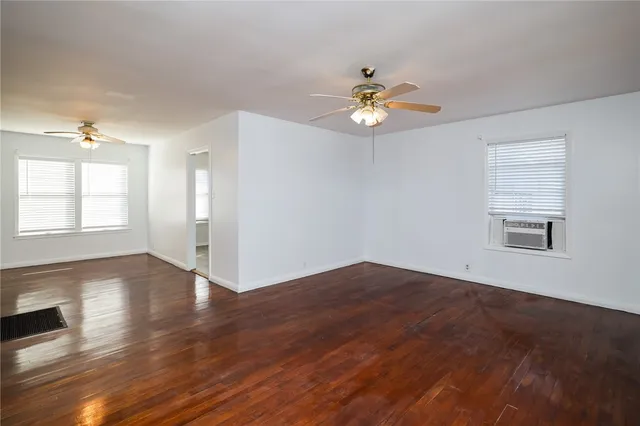 an empty room with wooden floor chandelier fan and windows
