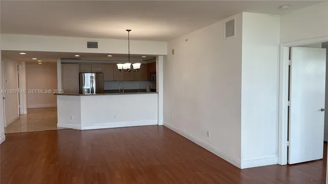 an empty room with wooden floor and kitchen view