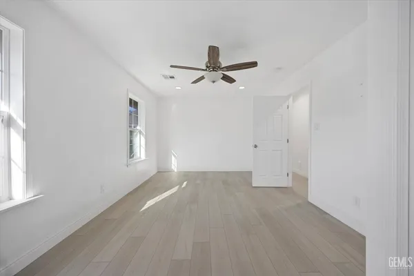 an empty room with wooden floor ceiling fan and windows