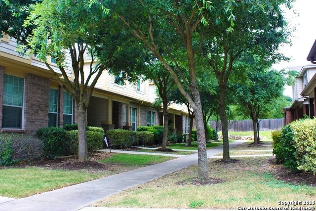 a view of a yard in front of a brick house with plants and large trees