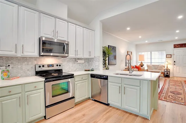 a kitchen with stainless steel appliances granite countertop a stove top oven a sink dishwasher and white cabinets with wooden floor