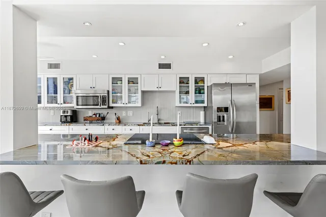 a kitchen with stainless steel appliances granite countertop a stove a sink a refrigerator and white cabinets with wooden floor