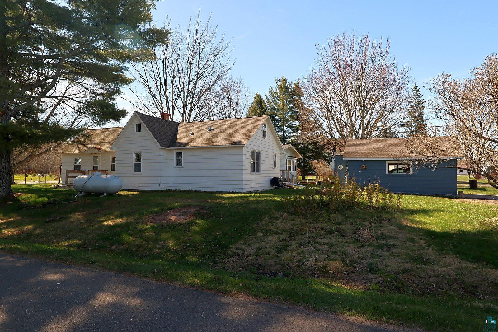 83185 Washington Avenue Port Wing, WI 54865 - Photo 2 of 26 Property exterior with white siding and brown shingle roof, complemented by a detached blue outbuilding