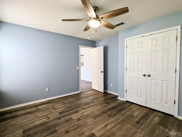 a view of an empty room with wooden floor and a ceiling fan