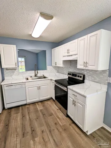 a white kitchen with a sink dishwasher stove and white cabinets with wooden floor