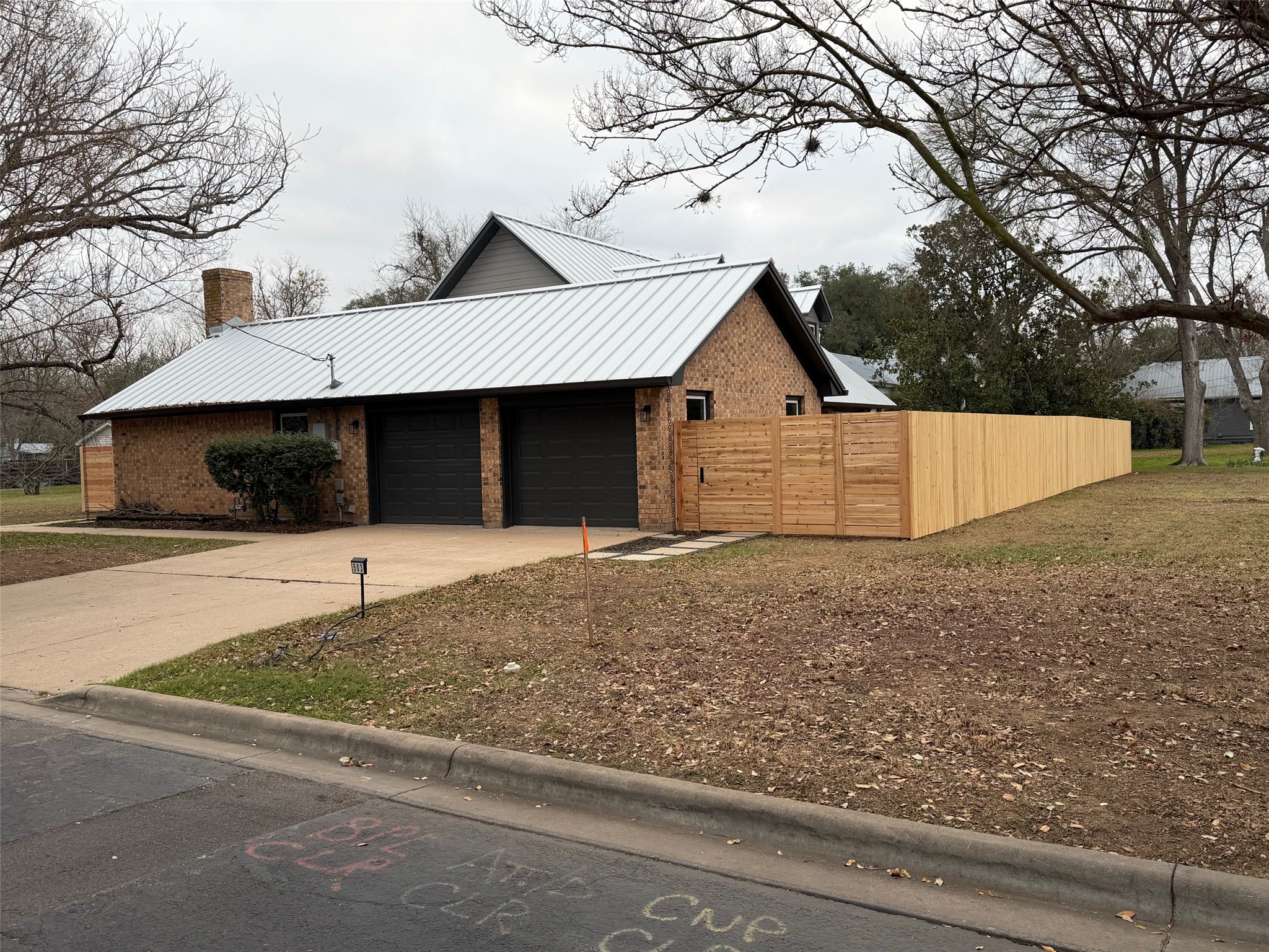 503 Elm Street Bastrop, TX 78602 - Photo 1 of 27 View of home's exterior featuring a chimney, brick siding, concrete driveway, a metal roof, and a garage