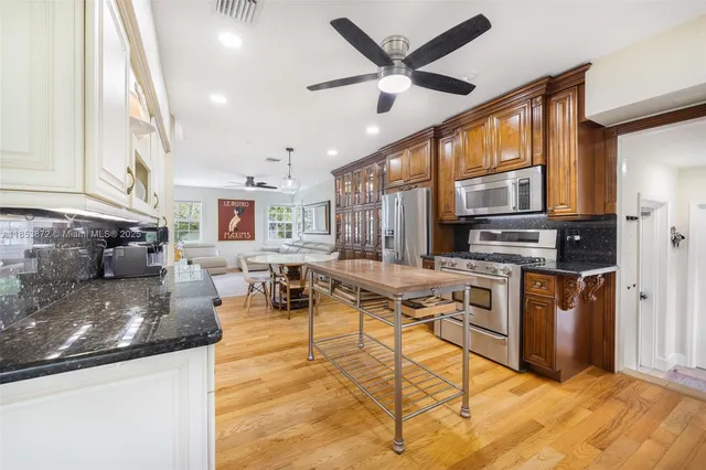 a living room with stainless steel appliances kitchen island granite countertop a stove a sink a refrigerator cabinets and a dining table with wooden floor