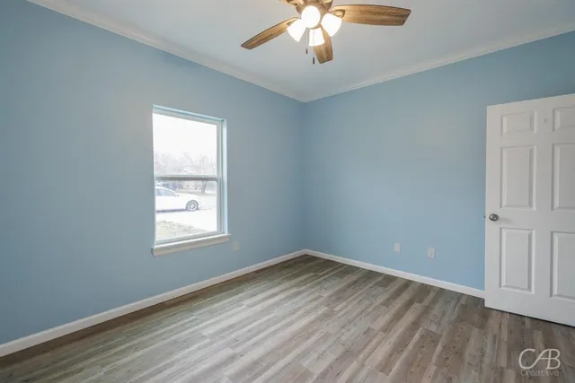 an empty room with wooden floor chandelier and windows