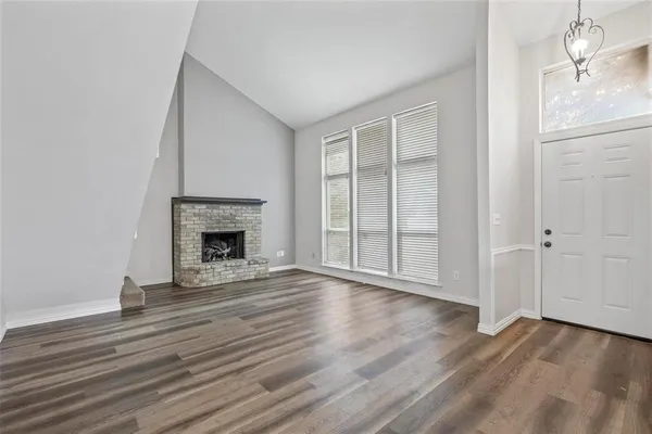 a view of an empty room with wooden floor fireplace and a window