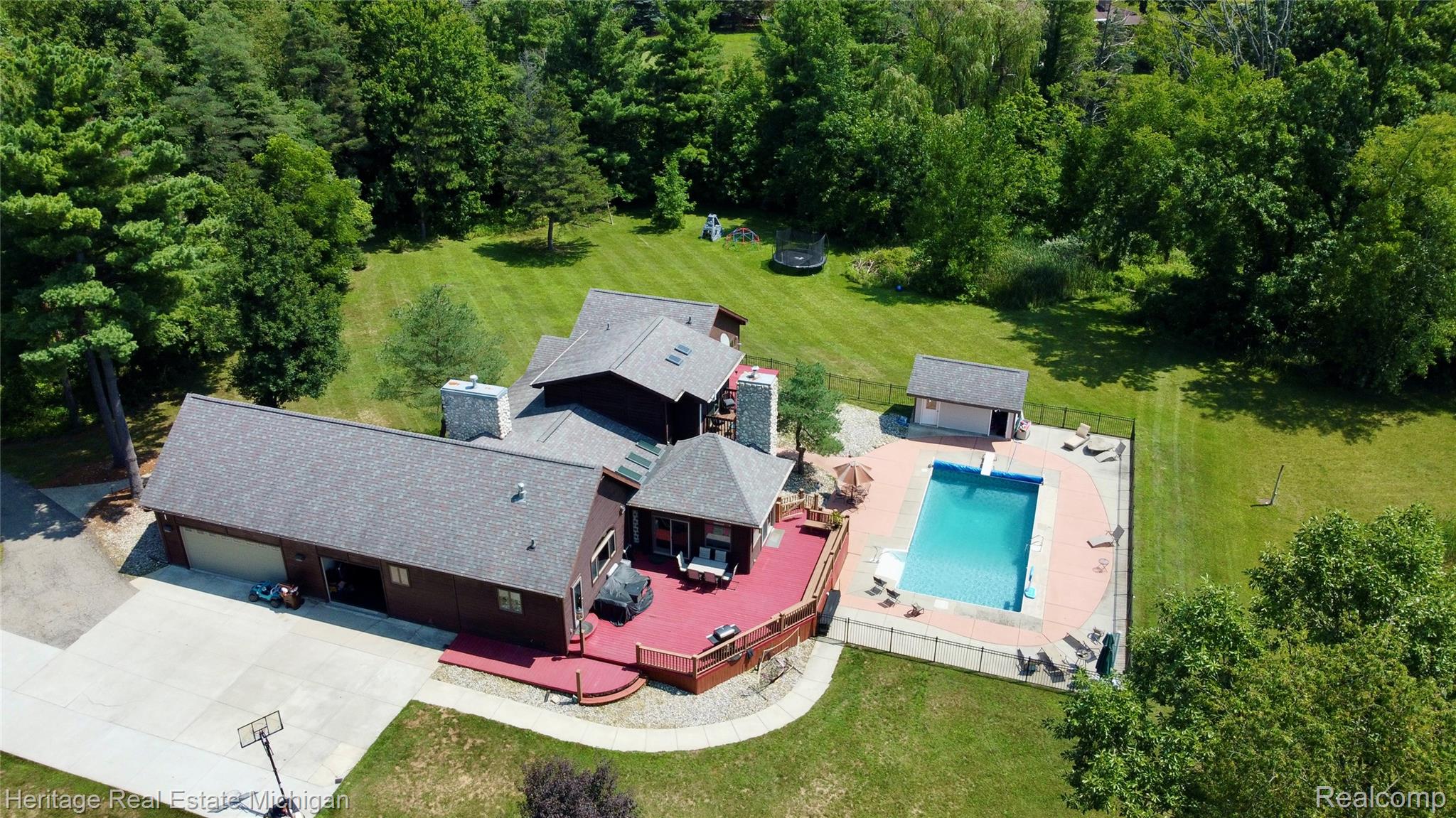 1888 Germany Road Williamston, MI 48895 - Photo 48 of 57 Expansive property featuring a multi-level home with a large attached garage, a spacious red deck, a fenced in-ground swimming pool, a pool house, and mature trees surrounding the perimeter
