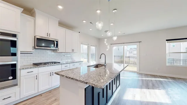 a kitchen with stainless steel appliances granite countertop a stove top oven a sink dishwasher and a microwave oven on the wooden floor