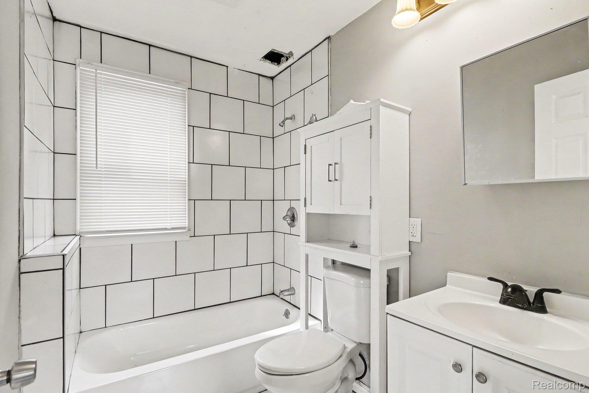 7743 Pitt Street Detroit, MI 48209 - Photo 14 of 15 Bathroom featuring white subway tile surround, bathtub, vanity with integrated sink, wall mirror, and an over-toilet storage cabinet