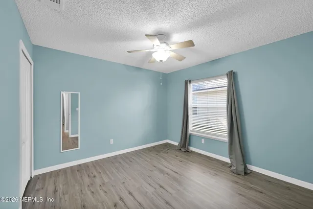 an empty room with wooden floor chandelier fan and windows