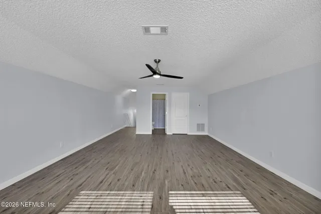 an empty room with wooden floor ceiling fan and windows