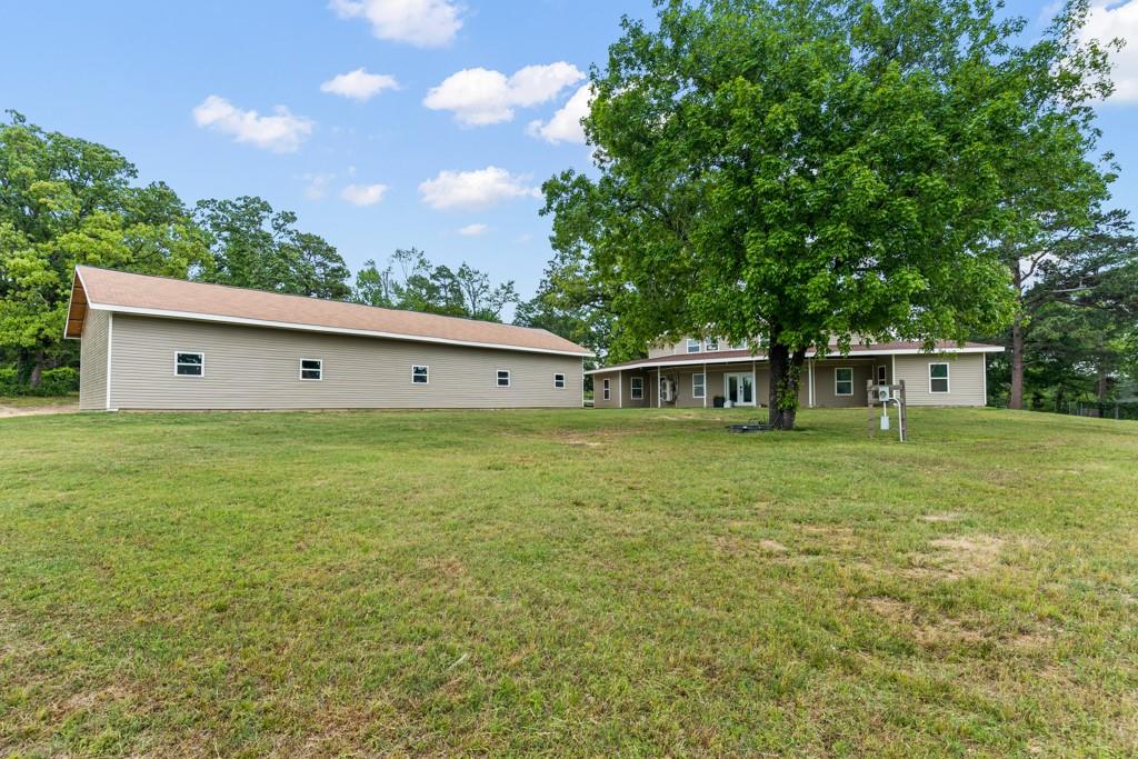 1129 Holly Road Gilmer, TX 75644 - Photo 31 of 31 Expansive grassy grounds featuring a secondary structure with a shed-style roof and multiple windows, alongside a main residence with a covered porch and double doors