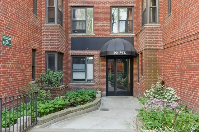 a view of a brick house with large windows and flower plants