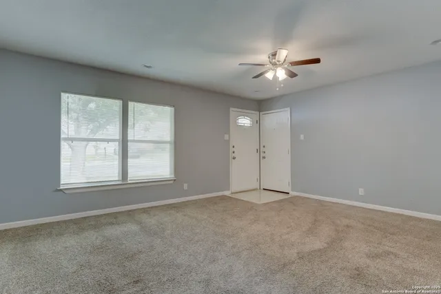 an empty room with chandelier fan and windows