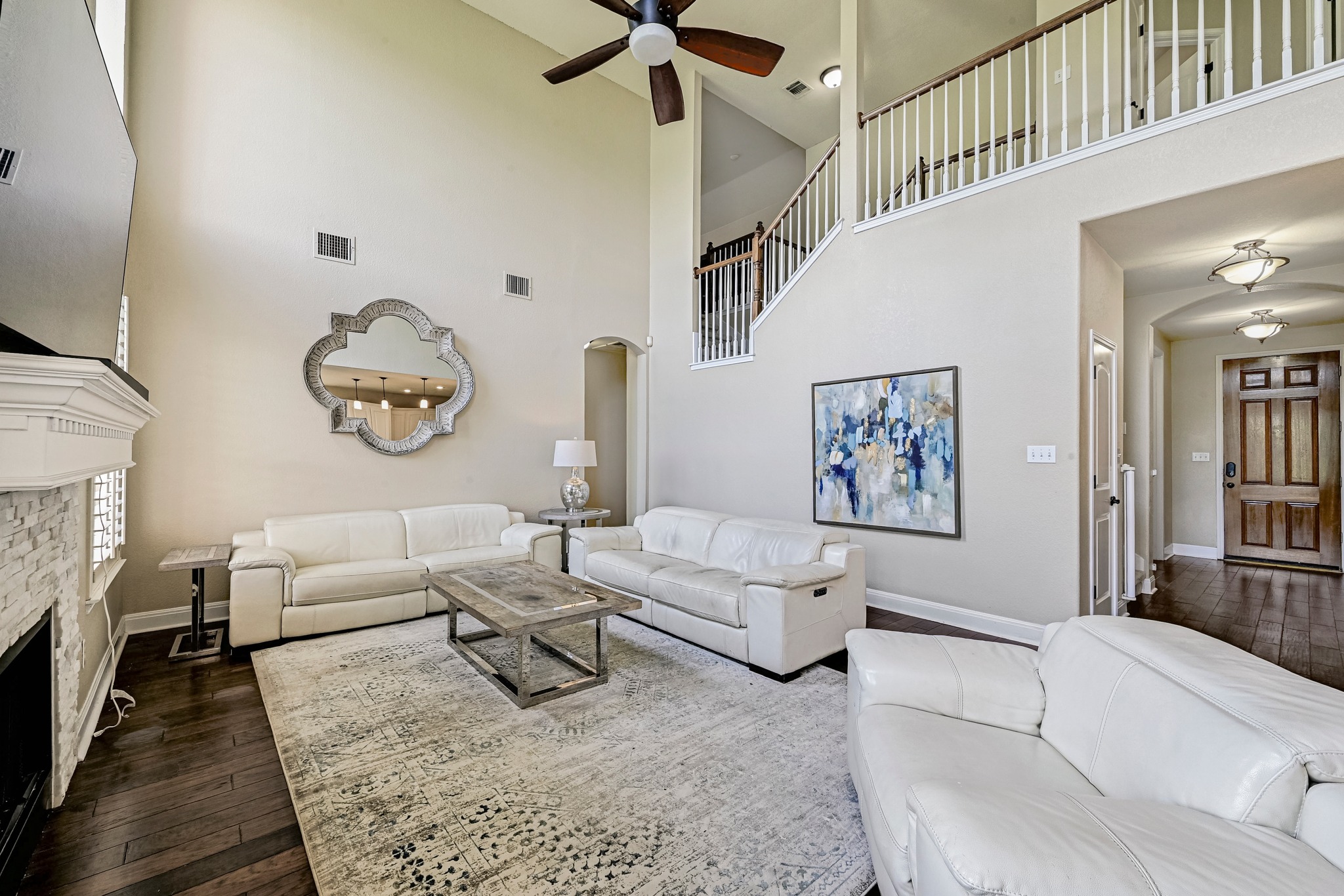 2408 Amen Corner Road Pflugerville, TX 78660 - Photo 8 of 40 Two-story living area featuring a stacked stone fireplace, dark wood-finish flooring, and a white baluster staircase