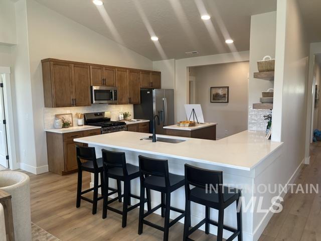 2035 Sumac Avenue Middleton, ID 83644 - Photo 4 of 17 Open-concept kitchen featuring wood-finish cabinetry, stainless steel appliances, a white subway tile backsplash, and a large central island with a sink and seating