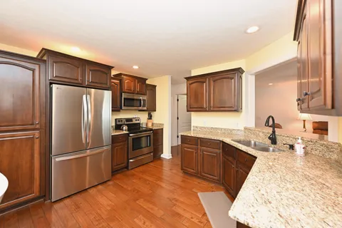 a large kitchen with stainless steel appliances granite countertop a refrigerator oven a sink dishwasher and wooden cabinets with wooden floor