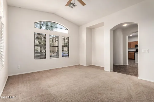an empty room with chandelier fan and windows