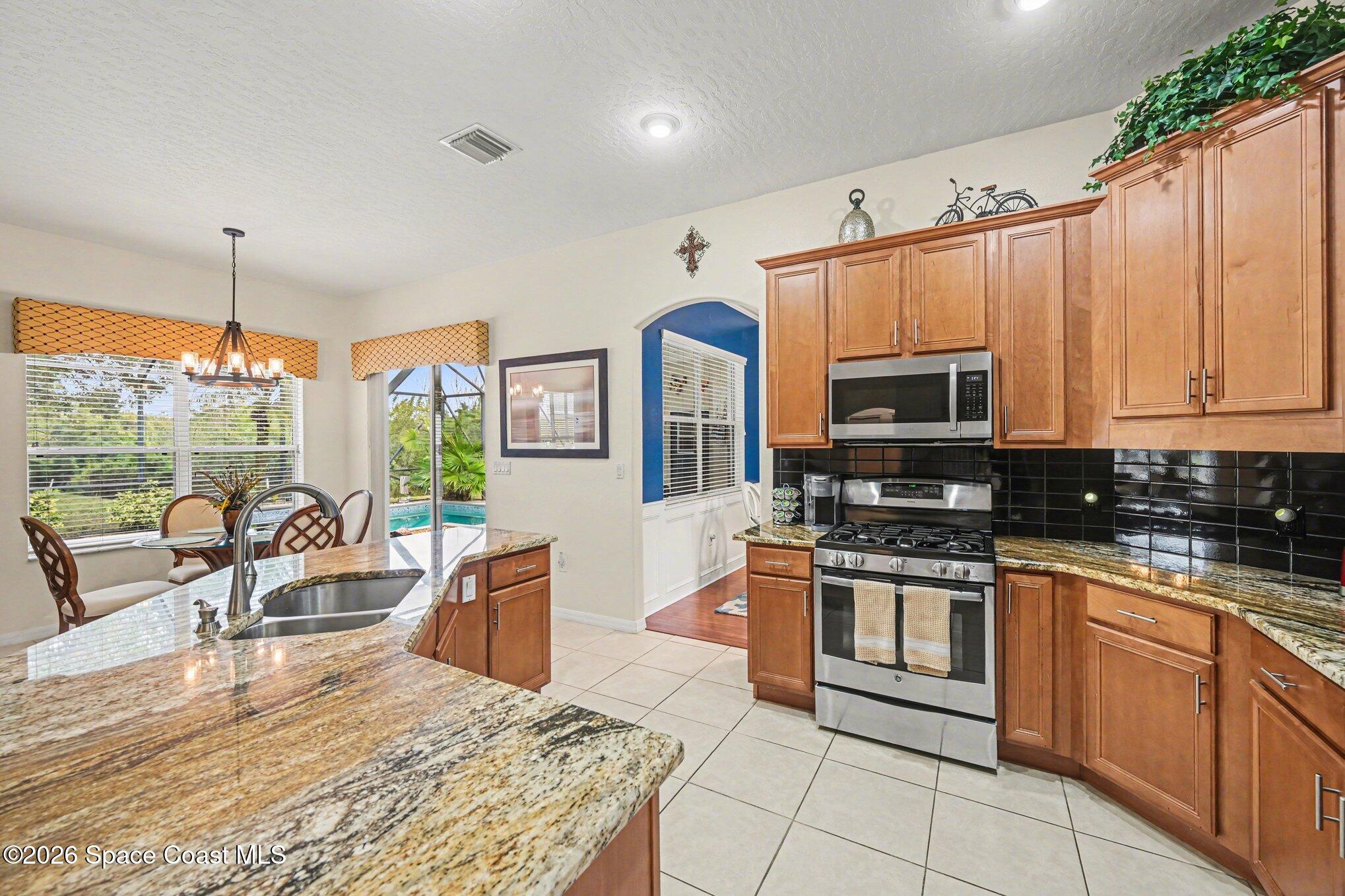 3760 Fringetree Lane Melbourne, FL 32940 - Photo 15 of 36 a kitchen with stainless steel appliances granite countertop a stove top oven a sink dishwasher a dining table and chairs with wooden floor
